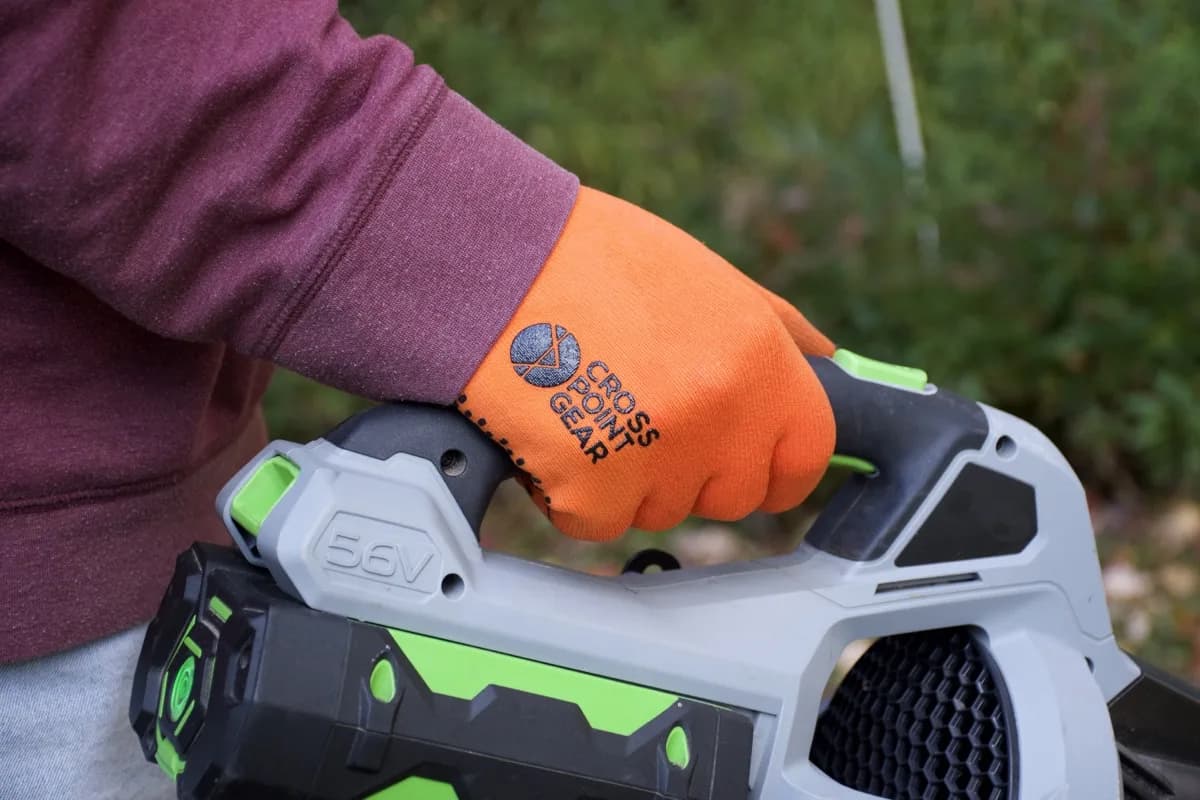 Cross Point Gear Sport Gloves — high-visibility orange waterproof work gloves with a coated grip palm, gripping the handle of a cordless outdoor power tool