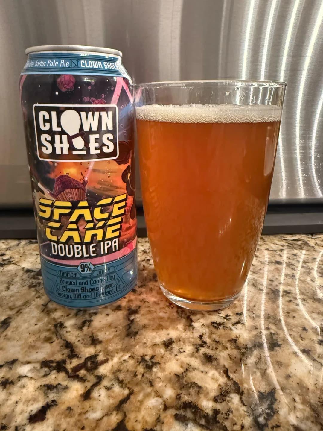 Clown Shoes Space Cake Double IPA can beside a poured hazy orange pint on a granite counter